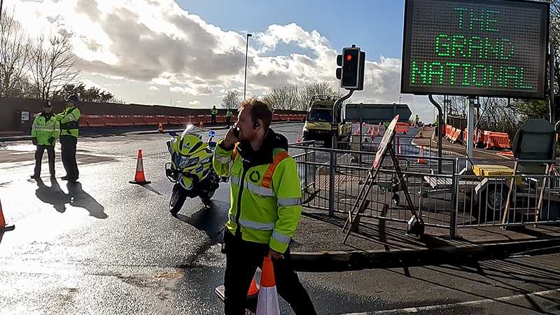 A man in a yellow vest is standing next to a sign