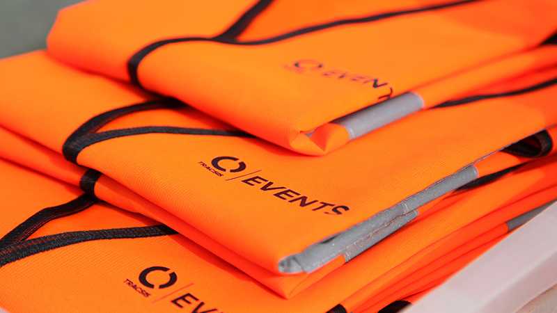 A stack of orange Tracsis Events branded high visibility jackets